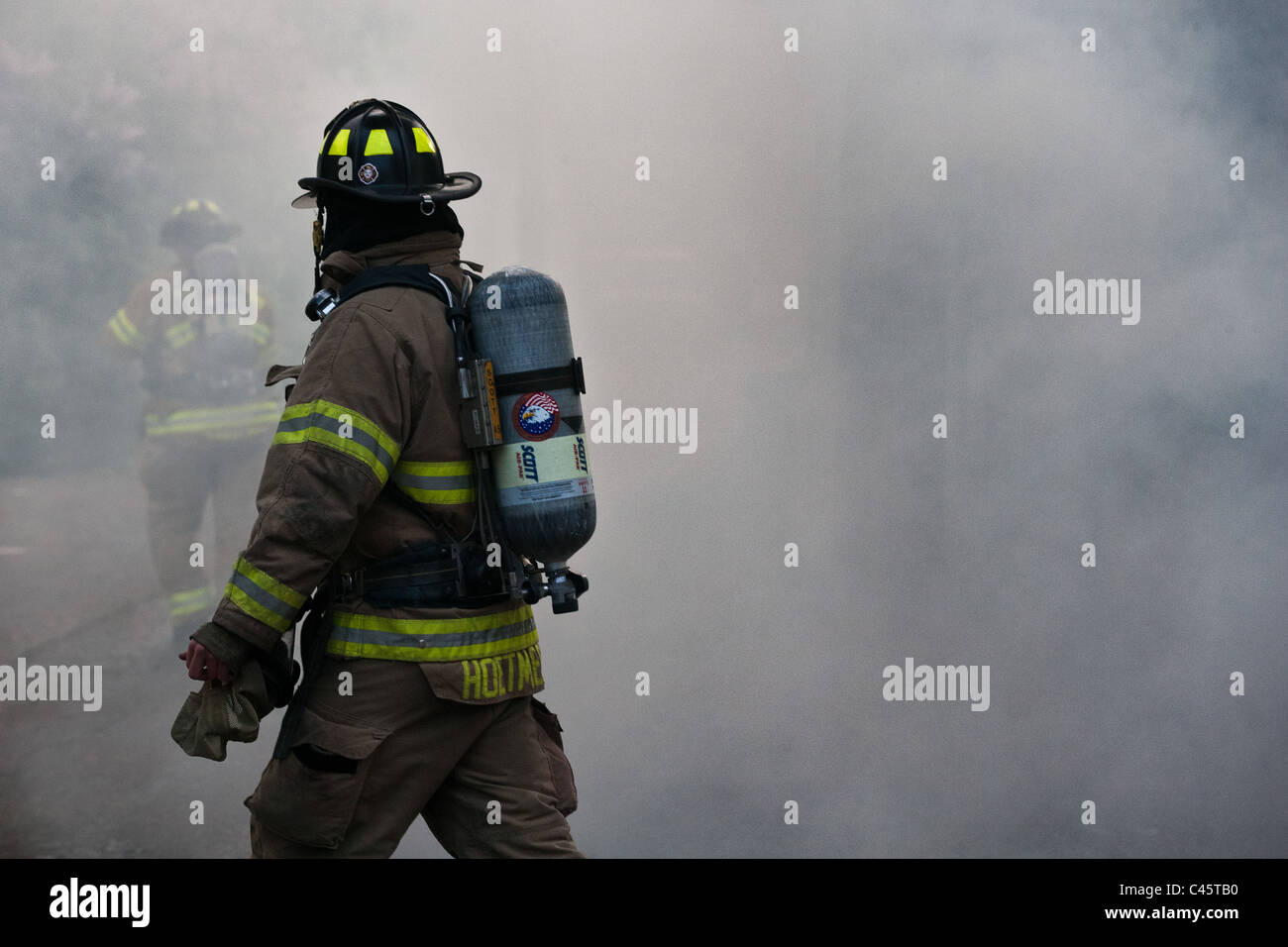 Vigile del fuoco nel fumo della casa di fuoco in pieno le attrezzature di protezione. Un secondo vigile del fuoco è visibile attraverso il fumo Foto Stock