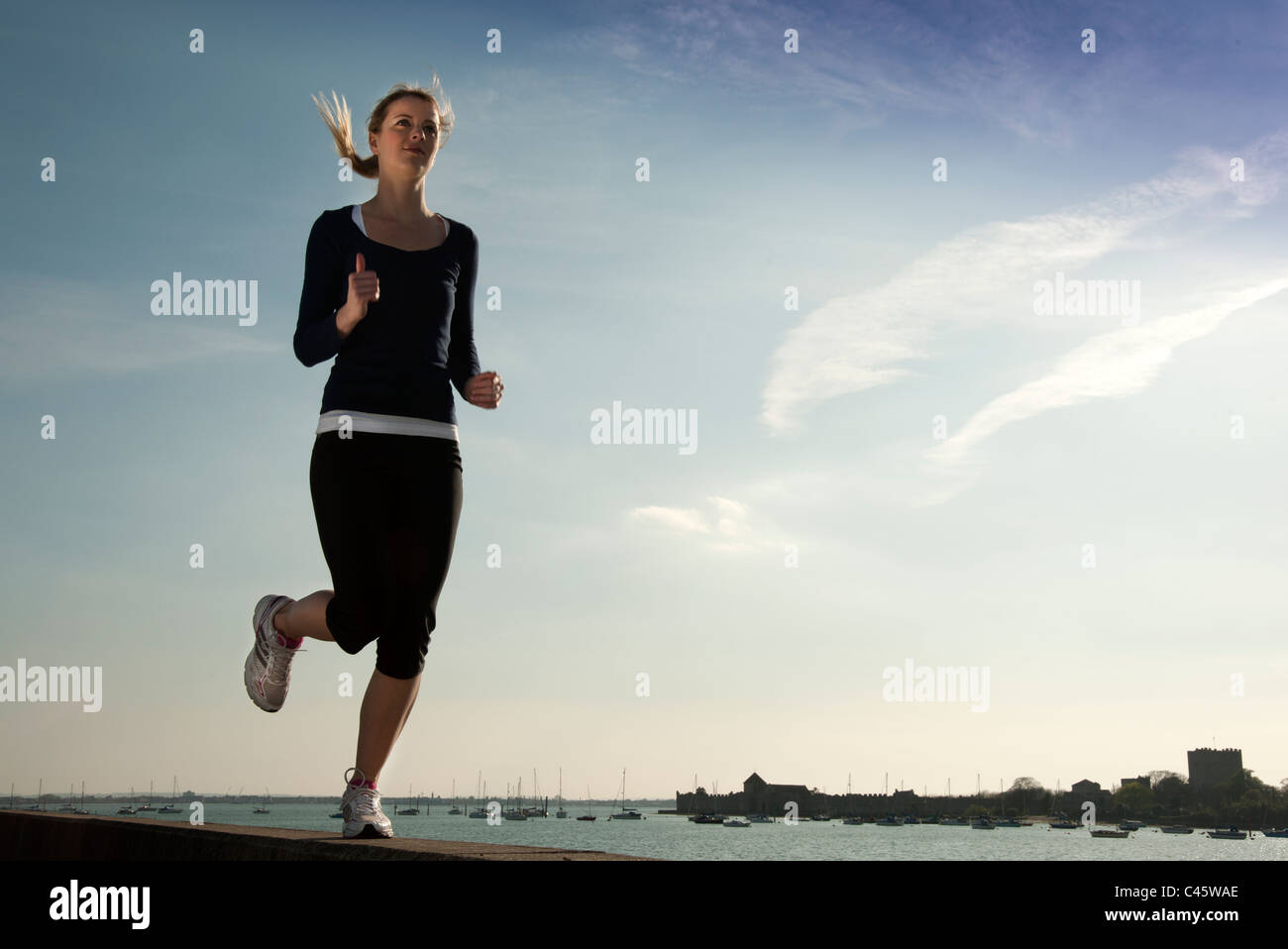 Donna che corre lungo il bordo delle acque sotto il sole Foto Stock