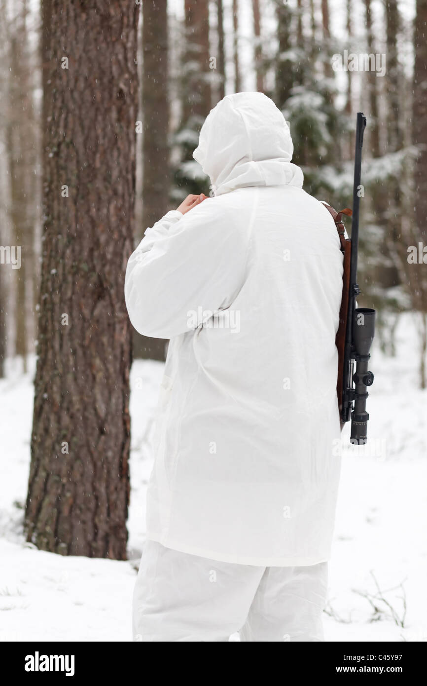 Soldato in bianco camouflage mirando con il fucile da cecchino a foresta d'inverno. Foto Stock