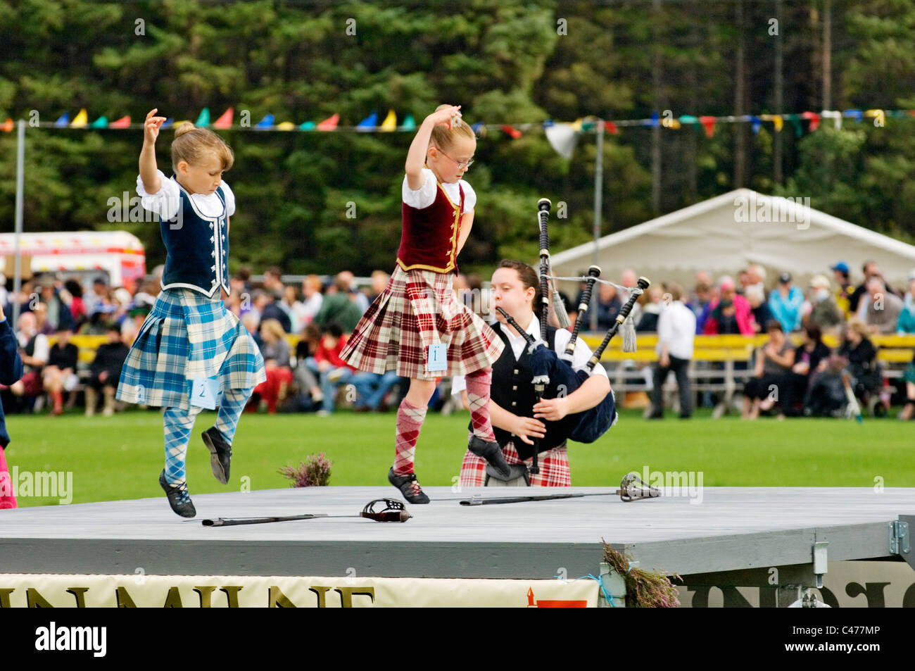 Lonach Highland Games a Strathdon, Grampian, Scozia. Piper gioca per le giovani ragazze di eseguire la tradizionale danza spada Foto Stock