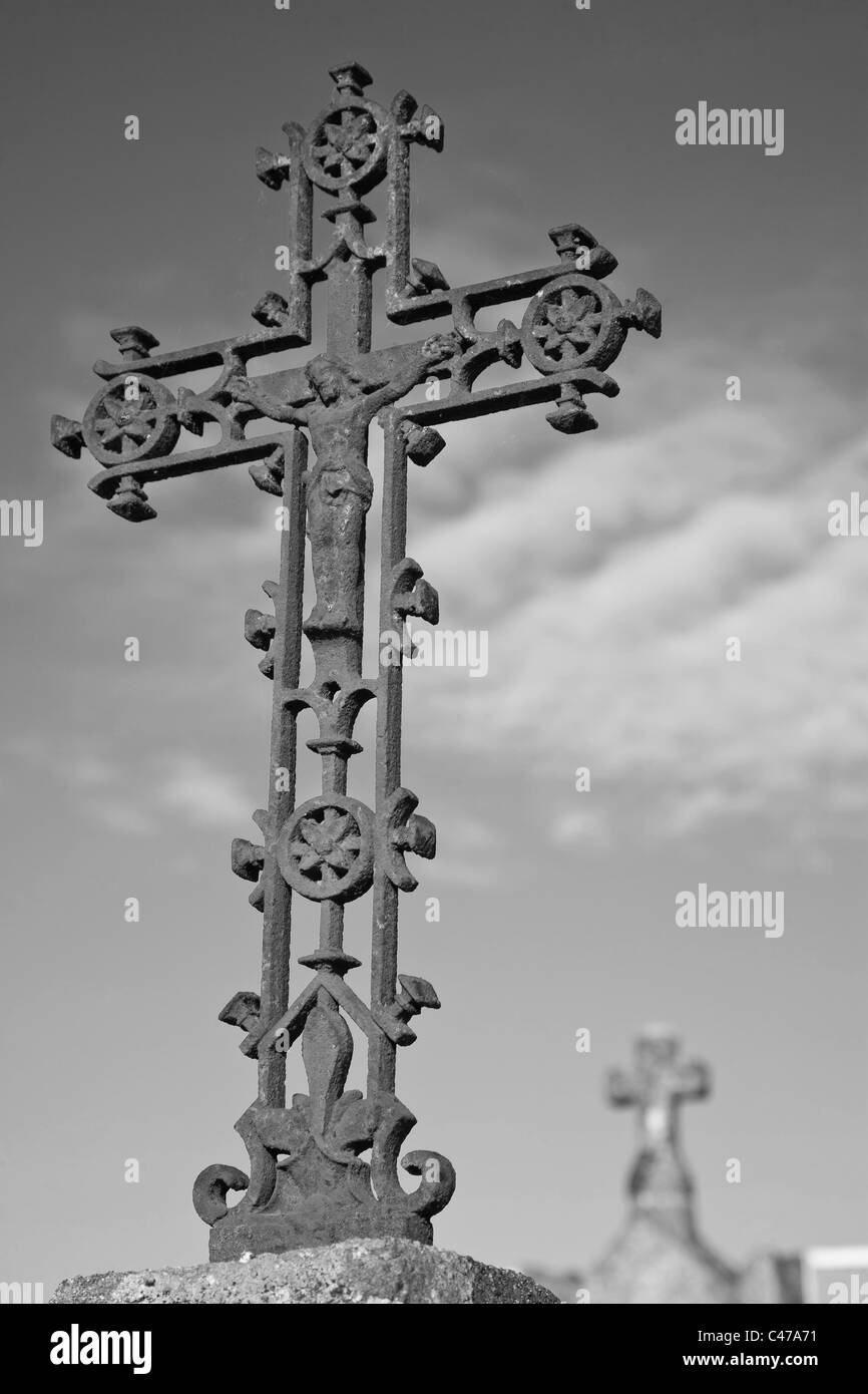 Un arrugginito croce decorativo con Gesù al centro contro il cielo con una croce di pietra in background Foto Stock