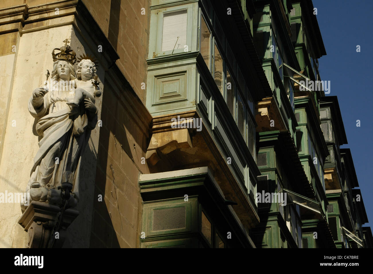 Un scolpito sculture religiose in corrispondenza della zona di spigolo di un edificio residenziale con i tipici balconi di legno a La Valletta la città capitale di Malta isola Foto Stock