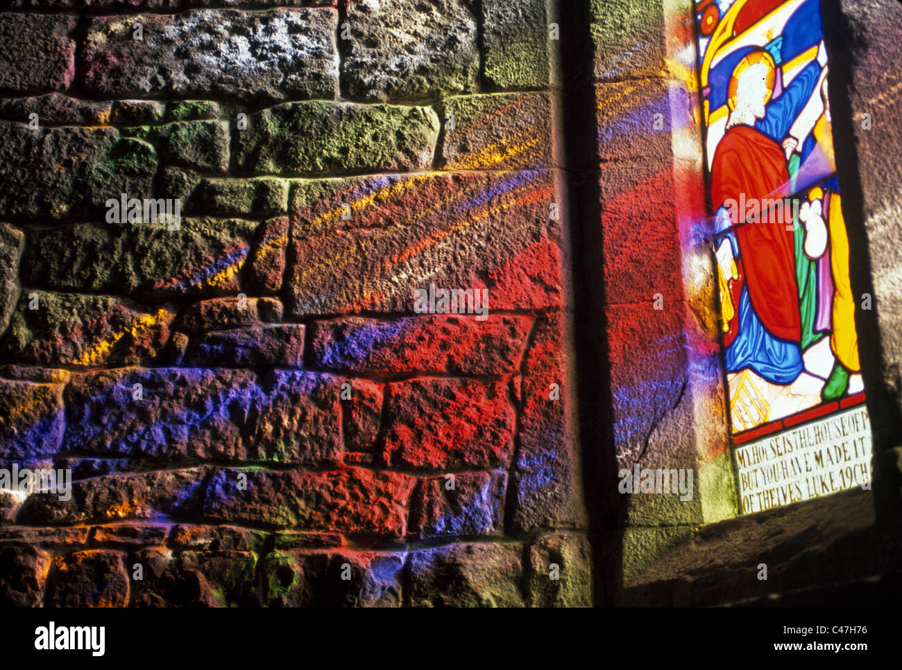Brillante luce solare rifratta attraverso una vetrata proietta pattern colorati sulla pianura muro di pietra di una vecchia chiesa a Adare, Irlanda. Foto Stock