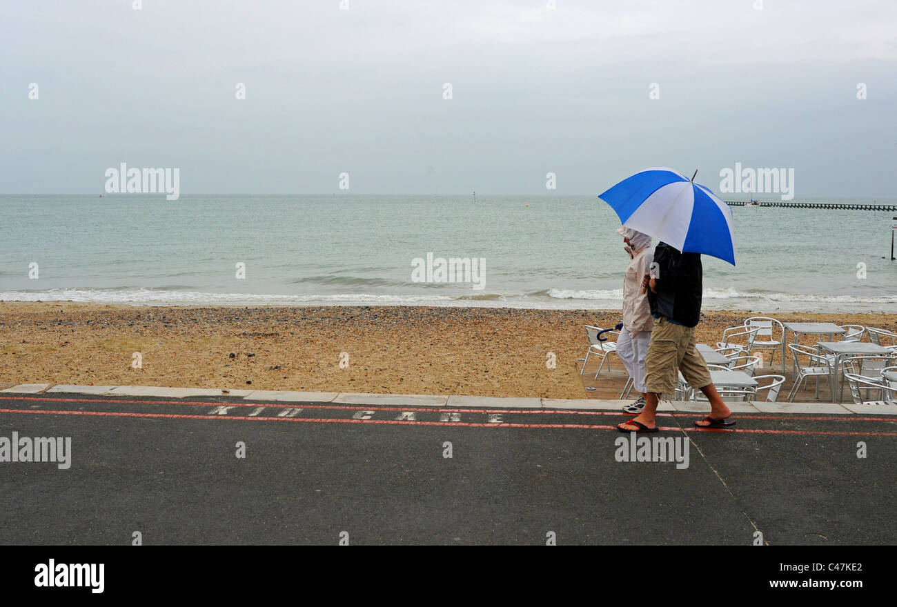 Giovane con grandi e luminose ombrellone a piedi lungo Littlehampton lungomare su un tipico British opaca giornata estiva sulla costa sud REGNO UNITO Foto Stock