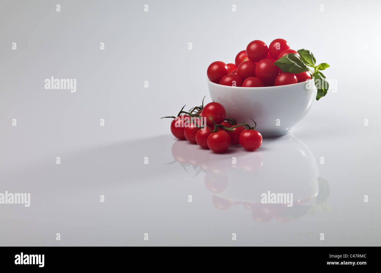Un bianco terrina di pomodori allegri con un rametto di basilico contro un semplice sfondo grigio Foto Stock