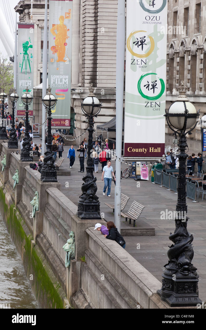 I pedoni a piedi passato il vecchio County Hall edificio con bandiere di pubblicità appesi da poli, Londra. Foto Stock