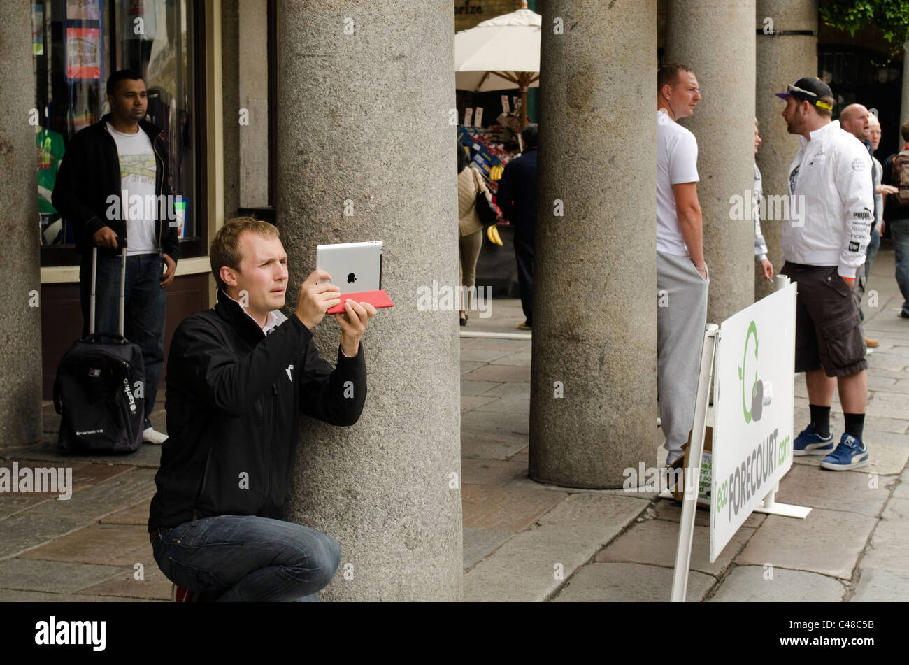 Giovane uomo 30s scattare fotografie con un iPad in Covent Garden Piazza alla partenza della Gumball Rally 3000 Foto Stock