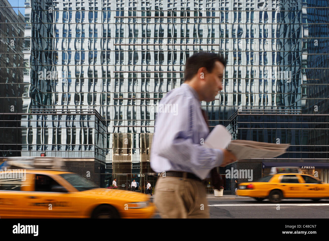 Un vetro riflettente facciata, taxi gialli e un uomo, New York City, Stati Uniti d'America Foto Stock
