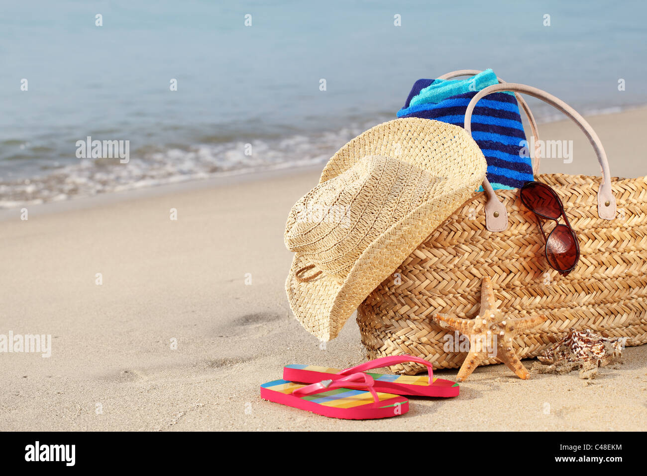 Estate borsa da spiaggia con cappello di paglia,asciugamano,occhiali da sole e flip flop sulla spiaggia sabbiosa Foto Stock