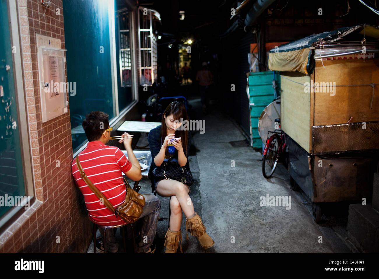 Mentre mangia con il suo ragazzo e una ragazza adolescente testi in un vicolo a Shilin Night Market, Taipei, Taiwan, Ottobre 23, 2010. Foto Stock