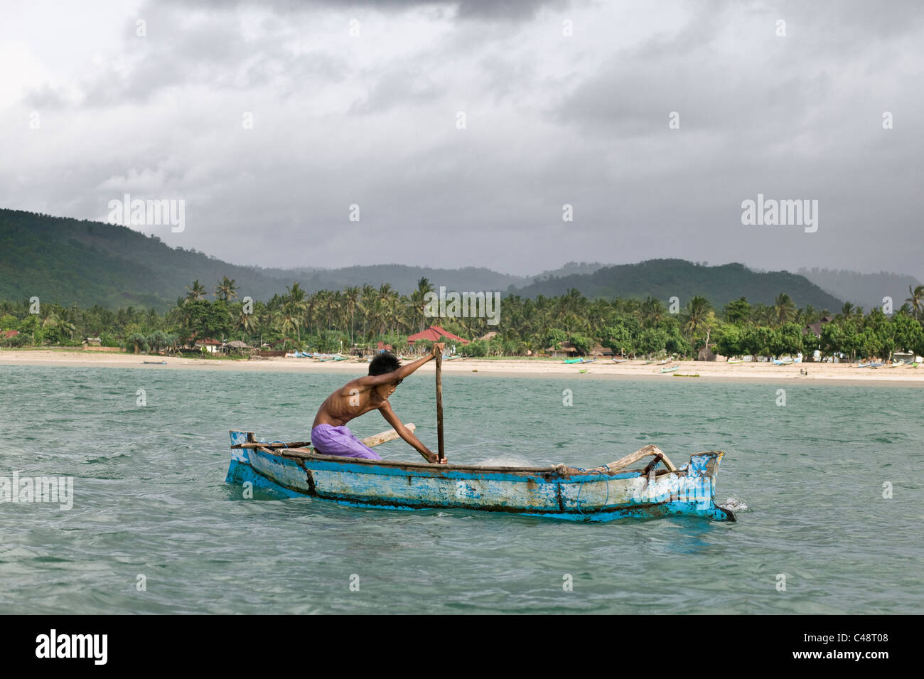 Un giovane pescatore pagaie la sua barca attraverso la baia di Kuta, Lombok, Indonesia. Foto Stock