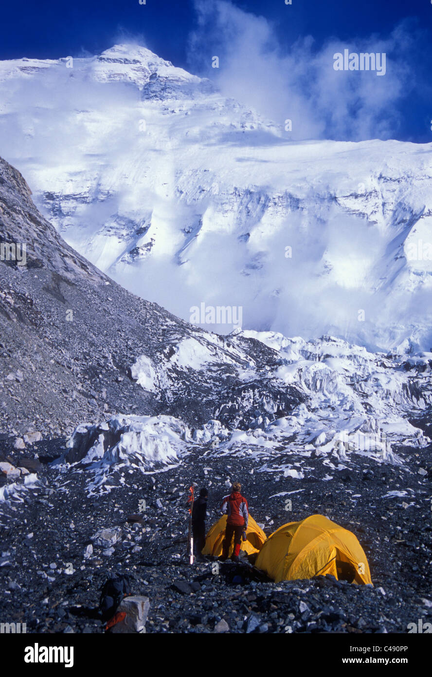 Due uomini stading al di fuori delle loro tende su un ghiacciaio, guardando le montagne coperte di neve. Foto Stock