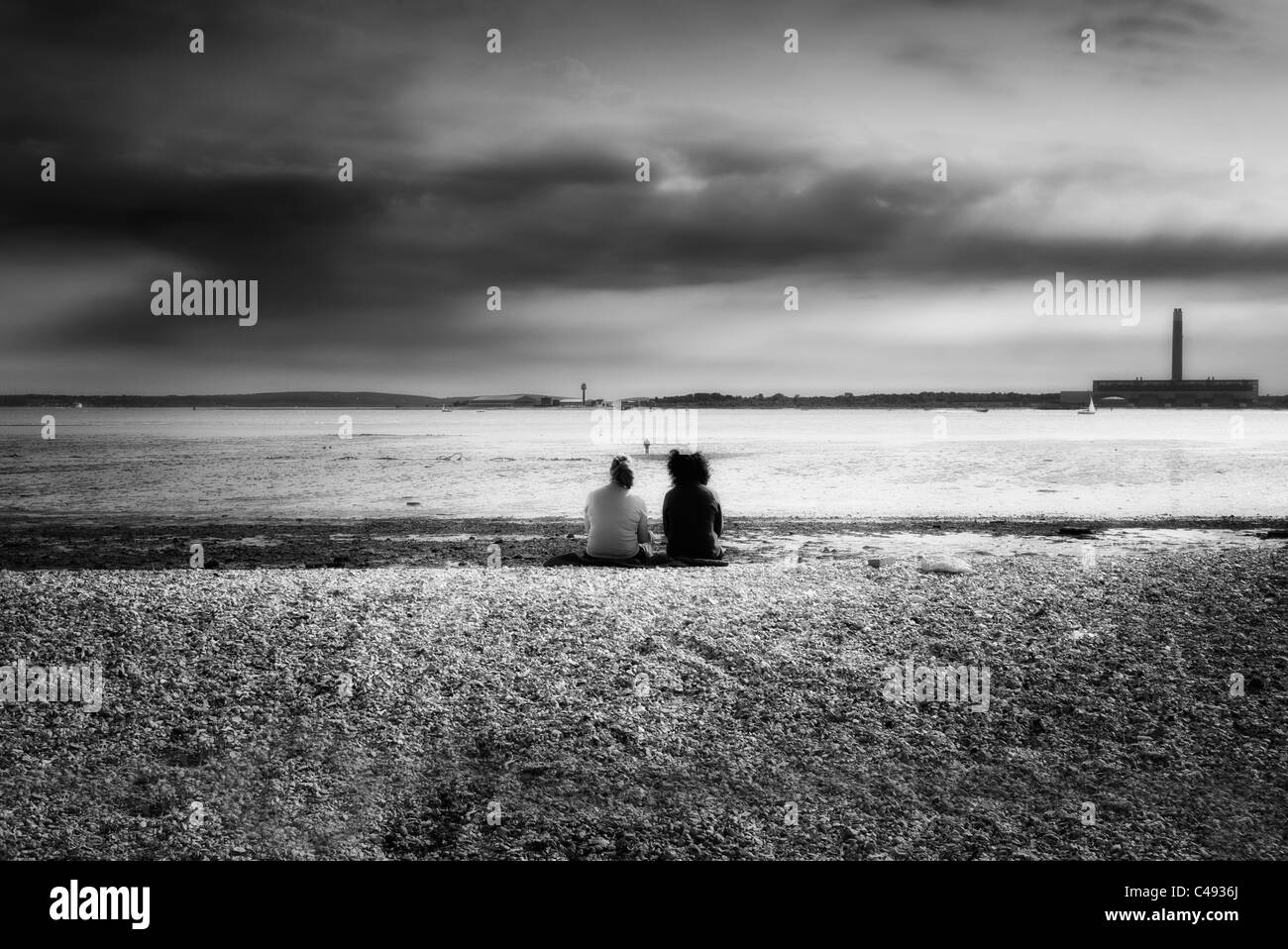 La gente seduta su di una spiaggia di ciottoli con la bassa marea a Southampton water REGNO UNITO in bianco e nero Foto Stock