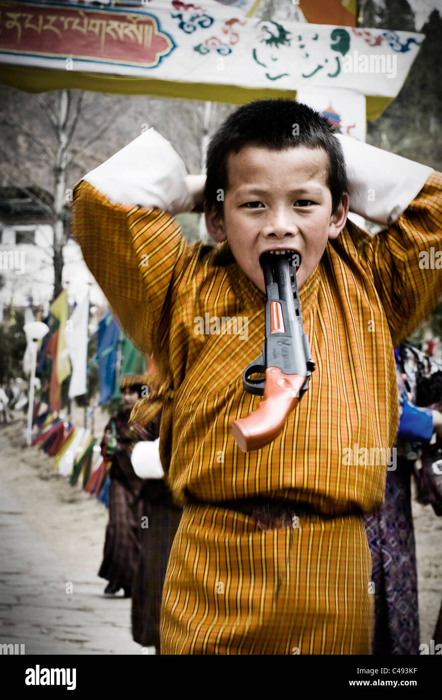 Un bambino bhutanesi in abito tradizionale pone con una pistola replica in un giorno di festa a Paro e. Foto Stock