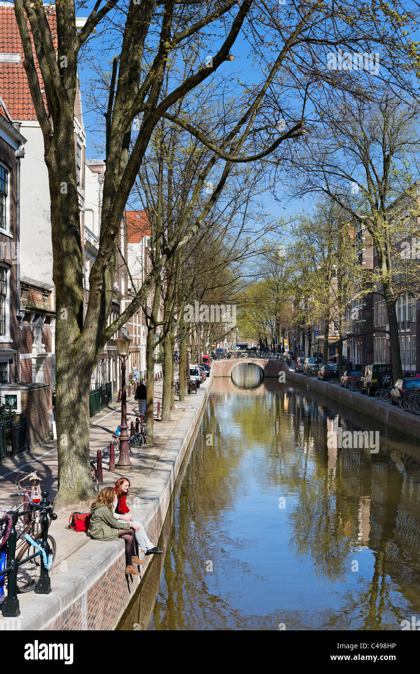 Due giovani donne sedute da Oudezijds Achterburgwal canal nel quartiere a luci rosse (de Wallen) in primavera, Amsterdam, Paesi Bassi Foto Stock