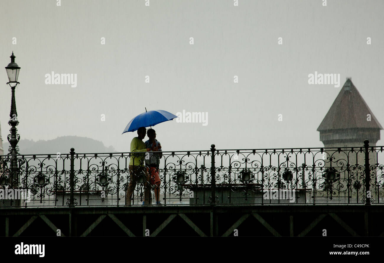 Due persone sotto un ombrello blu, attraversare un ponte a Lucerna, Svizzera, durante una tempesta di pioggia. Foto Stock