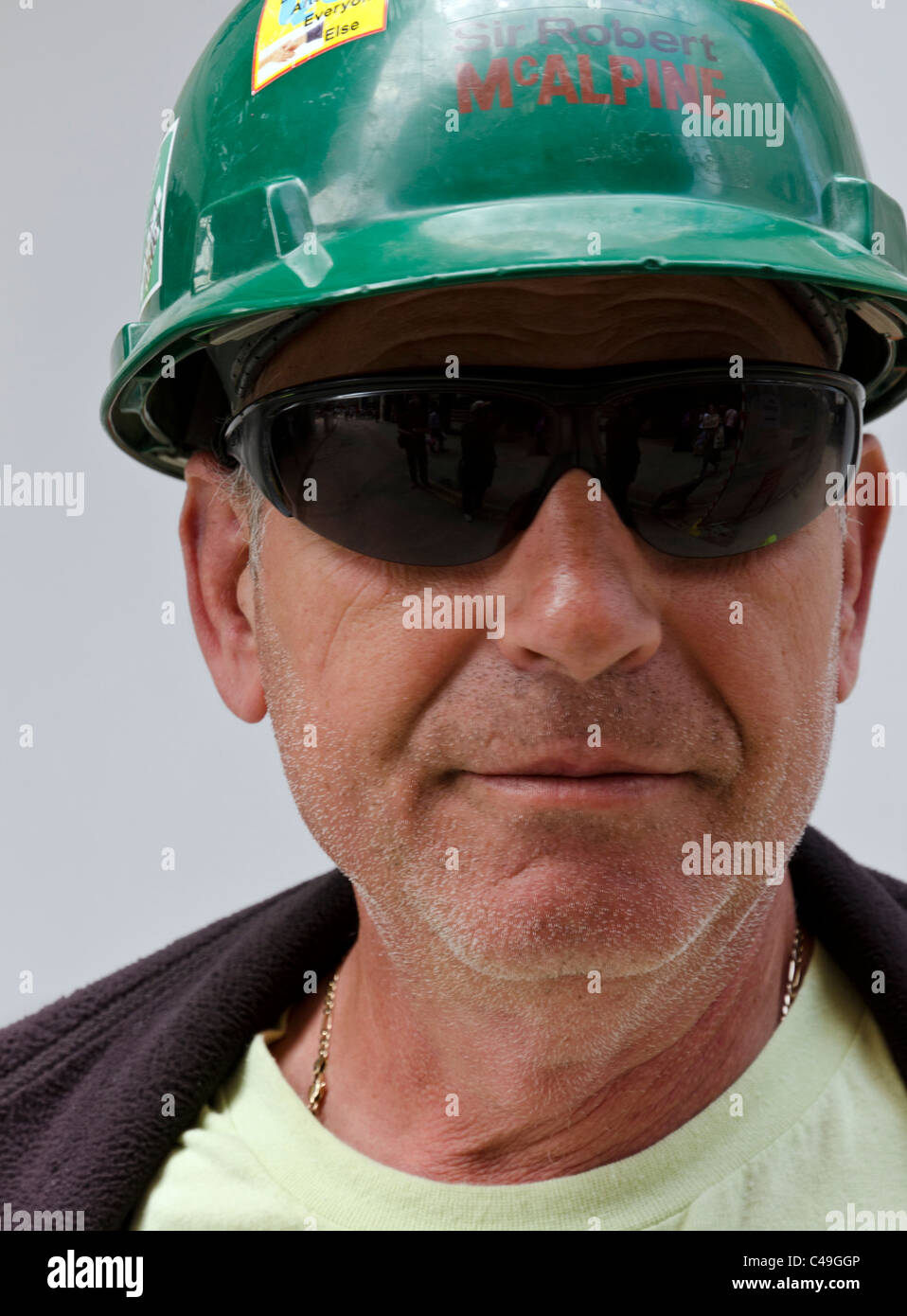 Ritratto di British lavoratore con casco verde e gli occhiali da sole sul sito con sfondo bianco, Londra, Inghilterra, Gran Bretagna, Regno Unito Foto Stock