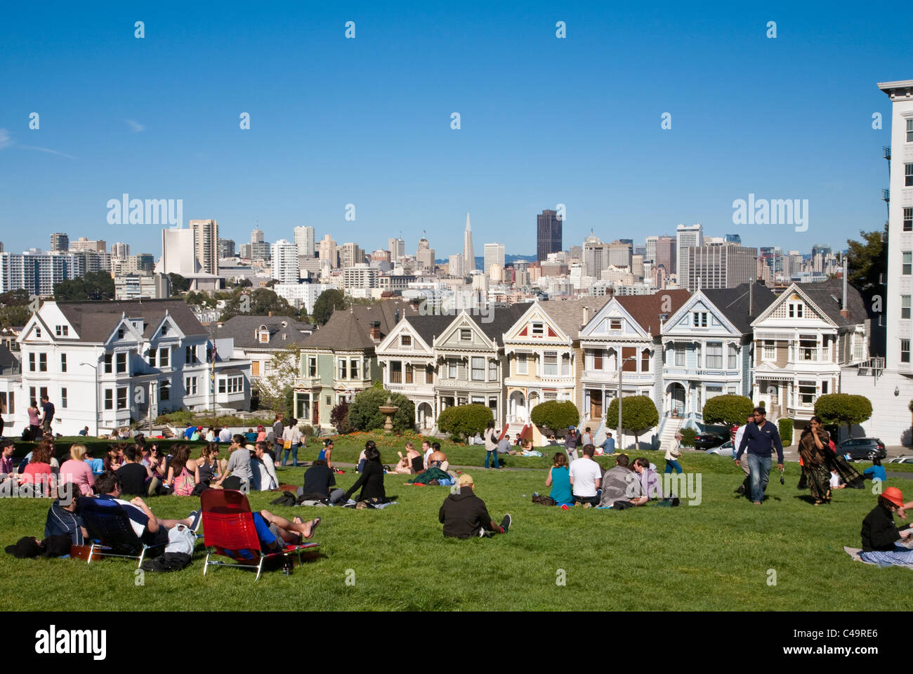 Cartolina di riga Painted Ladies case vittoriane attraverso da Alamo Square park su Steiner Street di San Francisco con lo skyline della città Foto Stock