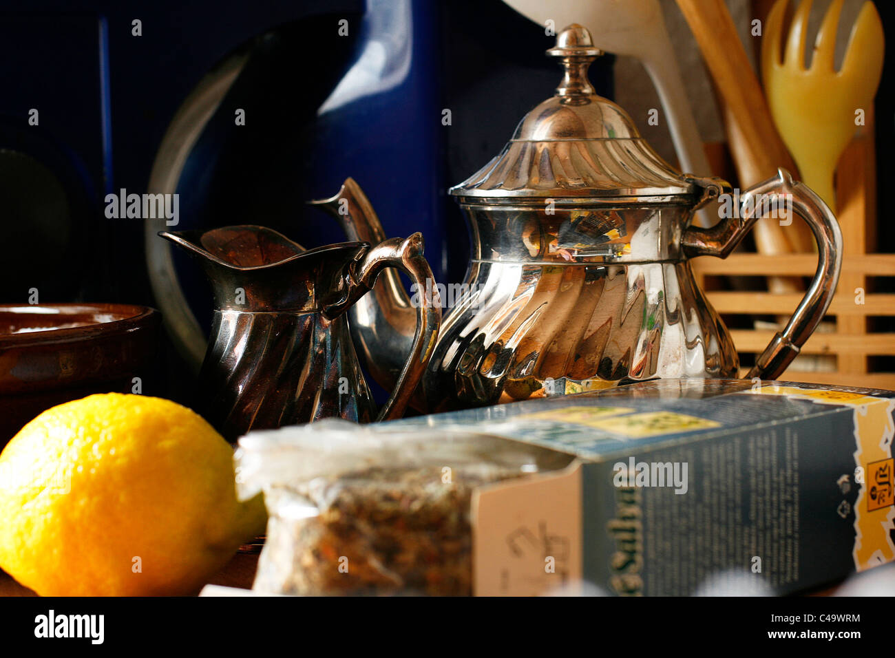Il tè alle erbe, una vecchia teiera in argento, un piccolo bricco per il latte e un limone di fronte all altra roba da cucina Foto Stock