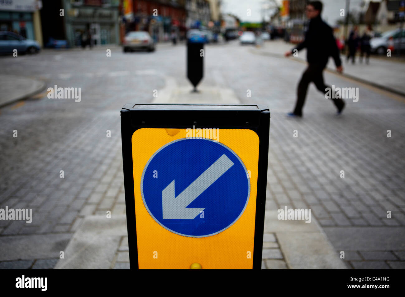 Un uomo attraversa una strada di fronte a tenere la sinistra bollard su una strada del Regno Unito Foto Stock