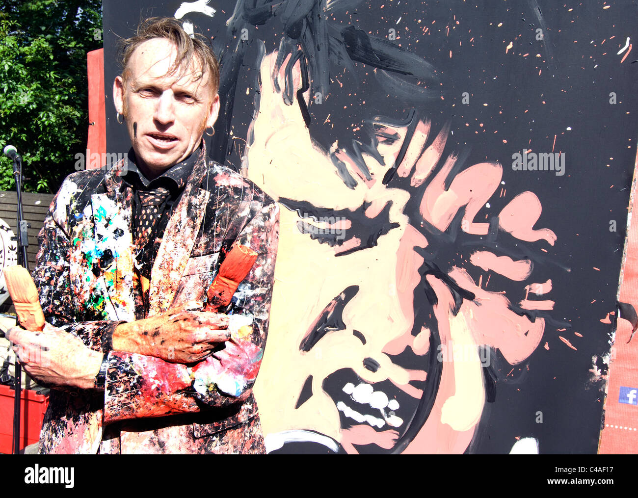 Artista, vestiti opener con vernice, spazzole di contenimento nella parte anteriore del canvas di Elvis ha dipinto in strada. Foto Stock