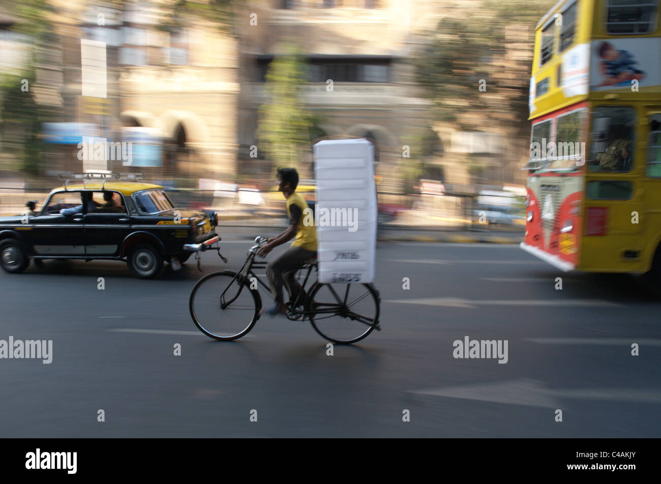 Un uomo su un molto carico bicicletta nel traffico di Bombay Foto Stock