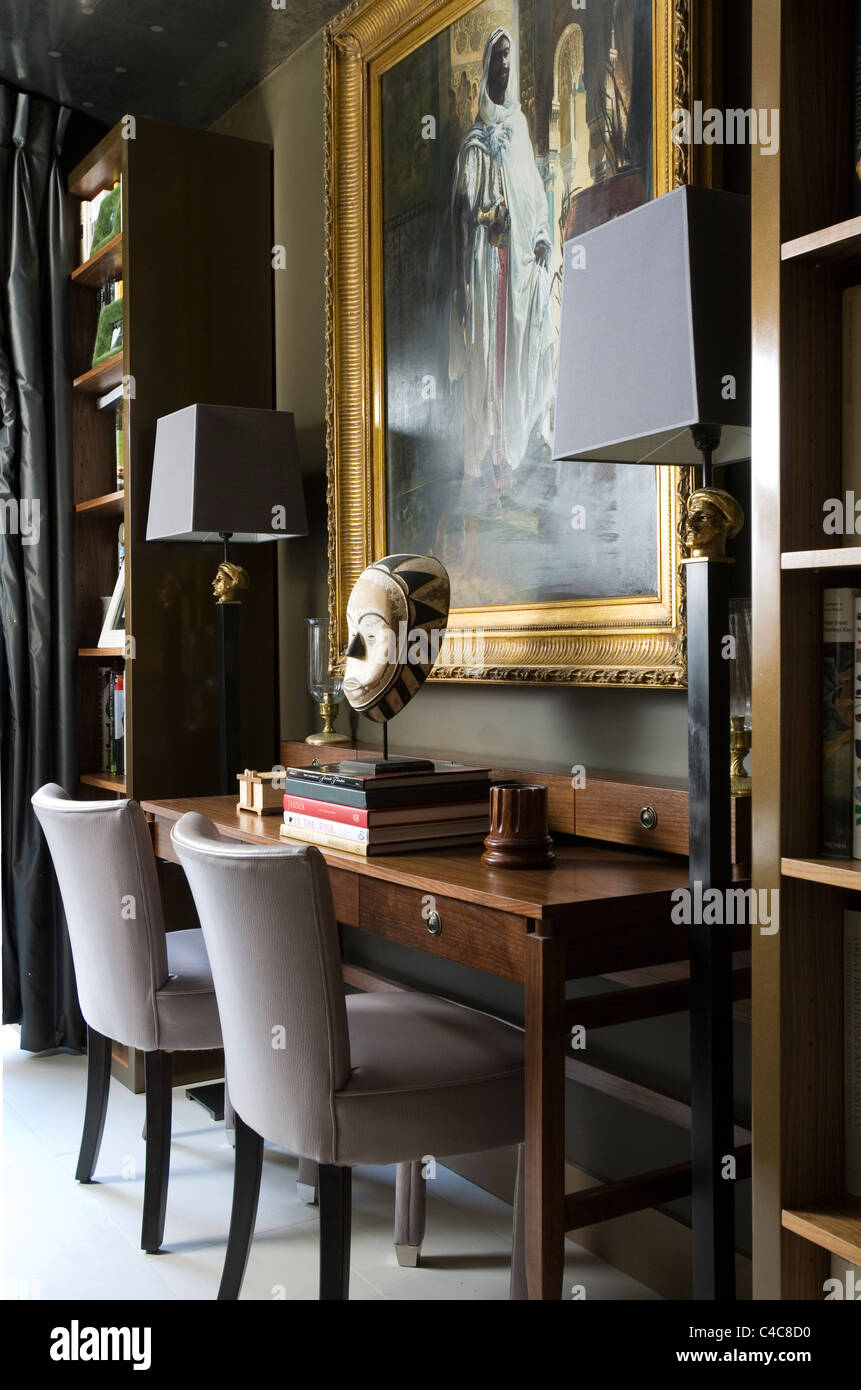 Con cornice dorata della pittura ad olio di legno sopra la scrivania con montata la maschera africana e sedie imbottite Foto Stock