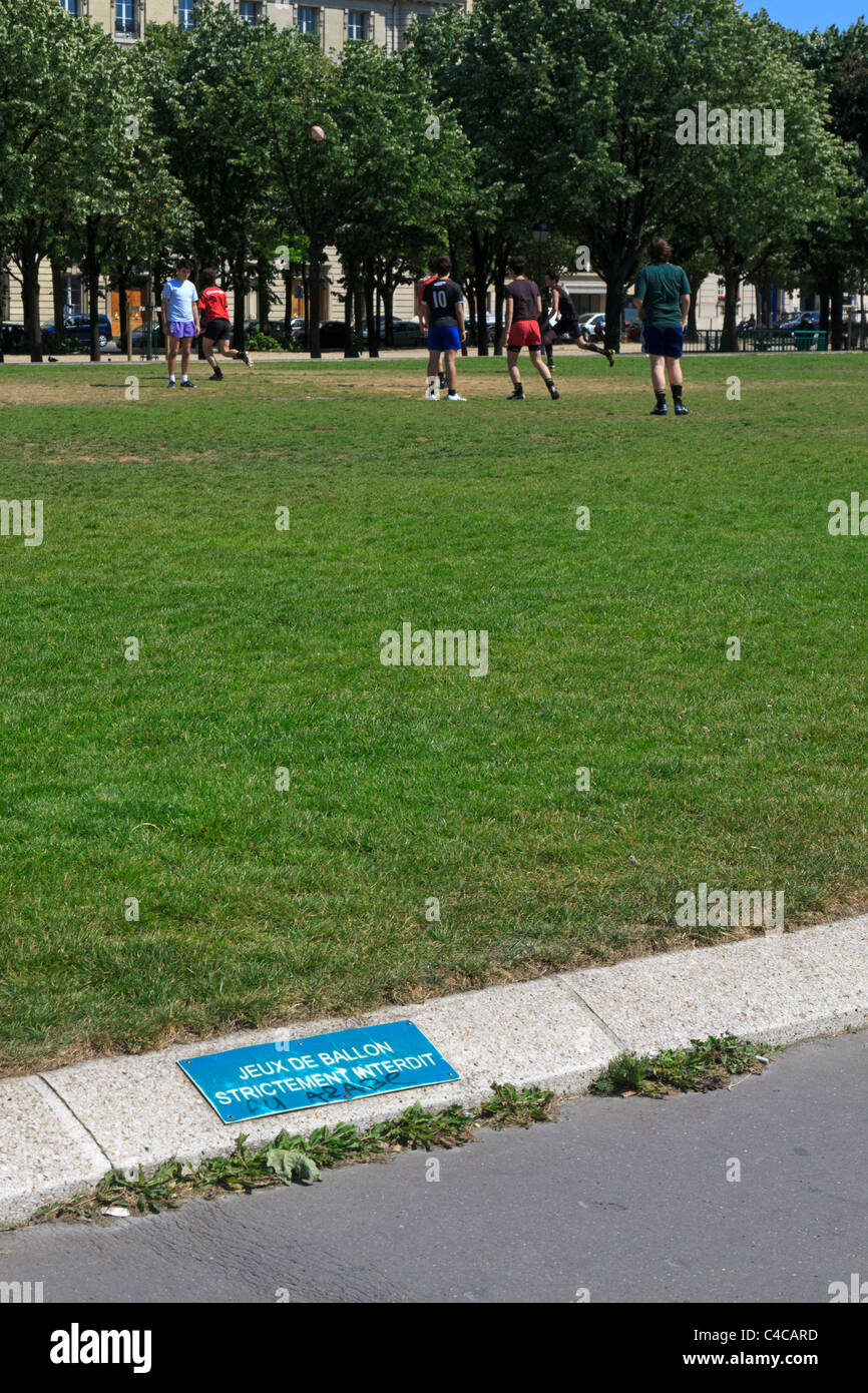 Un gruppo di giovani uomini giocare a calcio nel parco nonostante un avviso vietando giochi con la palla. Foto Stock