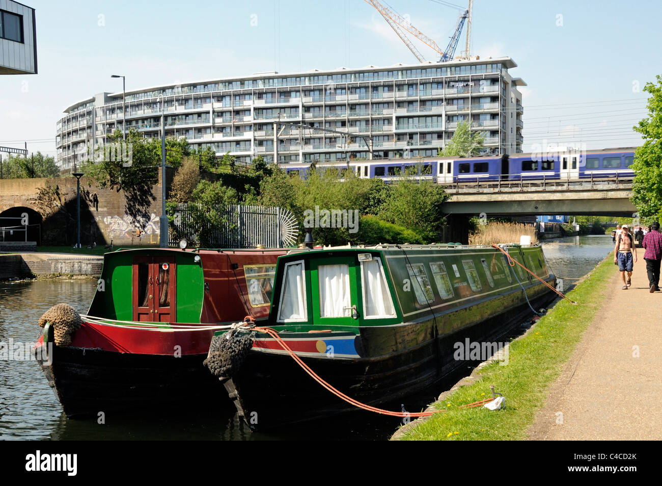 Case galleggianti sul Regent's Canal at Mile End con tow-percorso e il treno che va oltre il ponte con i moderni appartamenti dietro, London Inghilterra England Foto Stock