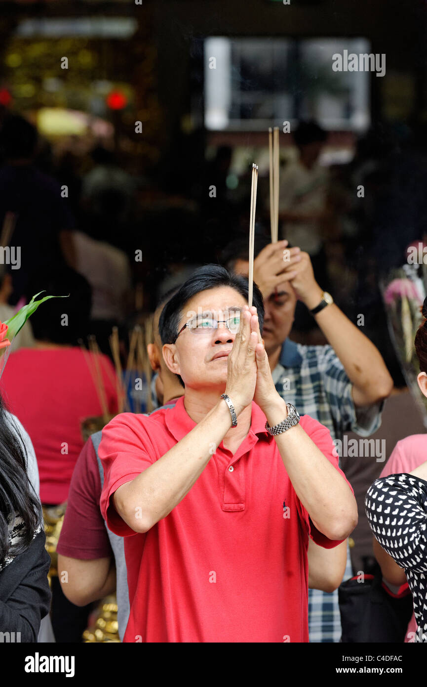 Mann tenendo un jos stick in silenziosa preghiera, tempio, Singapore, Asia Foto Stock