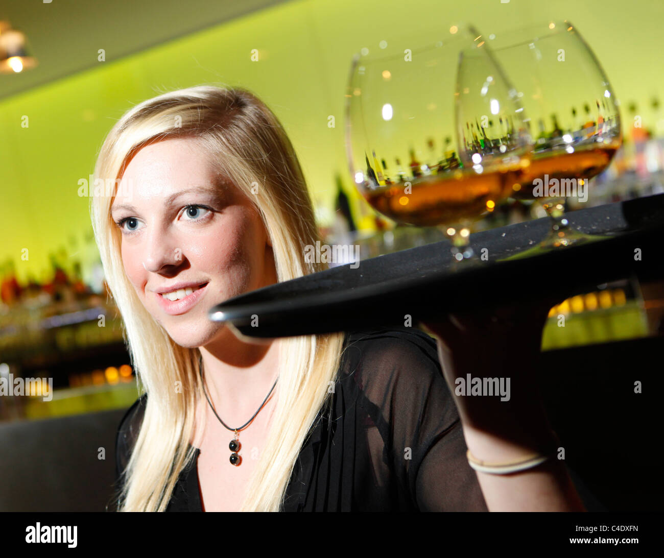 Cameriera in un cocktail bar che porta un vassoio di brandy bicchieri a palloncino Foto Stock