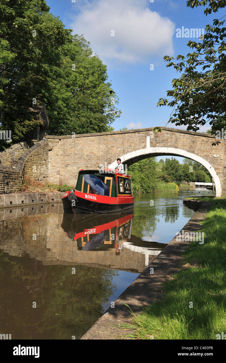 Un giorno di canal narrowboat noleggio passa sotto un ponte in pietra Kildwick, North Yorkshire, Inghilterra, Regno Unito Foto Stock