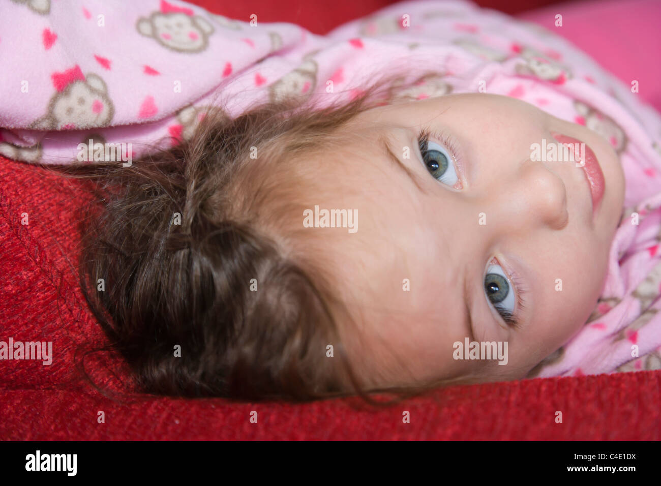 4 anni ragazza in rosa pigiama sdraiato sul divano rosso bed Foto Stock