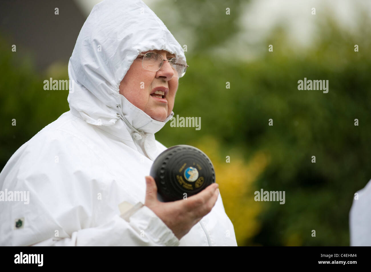 Una femmina di prato giocatore di bocce in bicchieri e wet weather marcia durante un pomeriggio piovoso bocce corrispondono Foto Stock