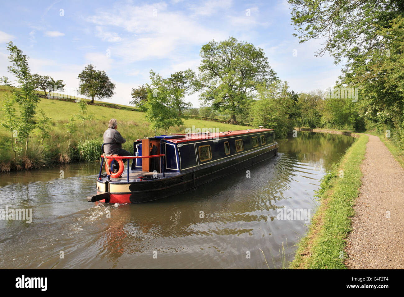 Un uomo manzi il suo stretto canale barca lungo il Leeds e Liverpool canal vicino a Skipton, nello Yorkshire, Inghilterra, Regno Unito Foto Stock