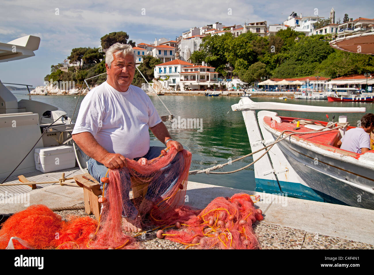 Anziano pescatore riparando il suo net presso il vecchio porto di Skiathos, isola Skiathos, Sporadi settentrionali, Grecia Foto Stock