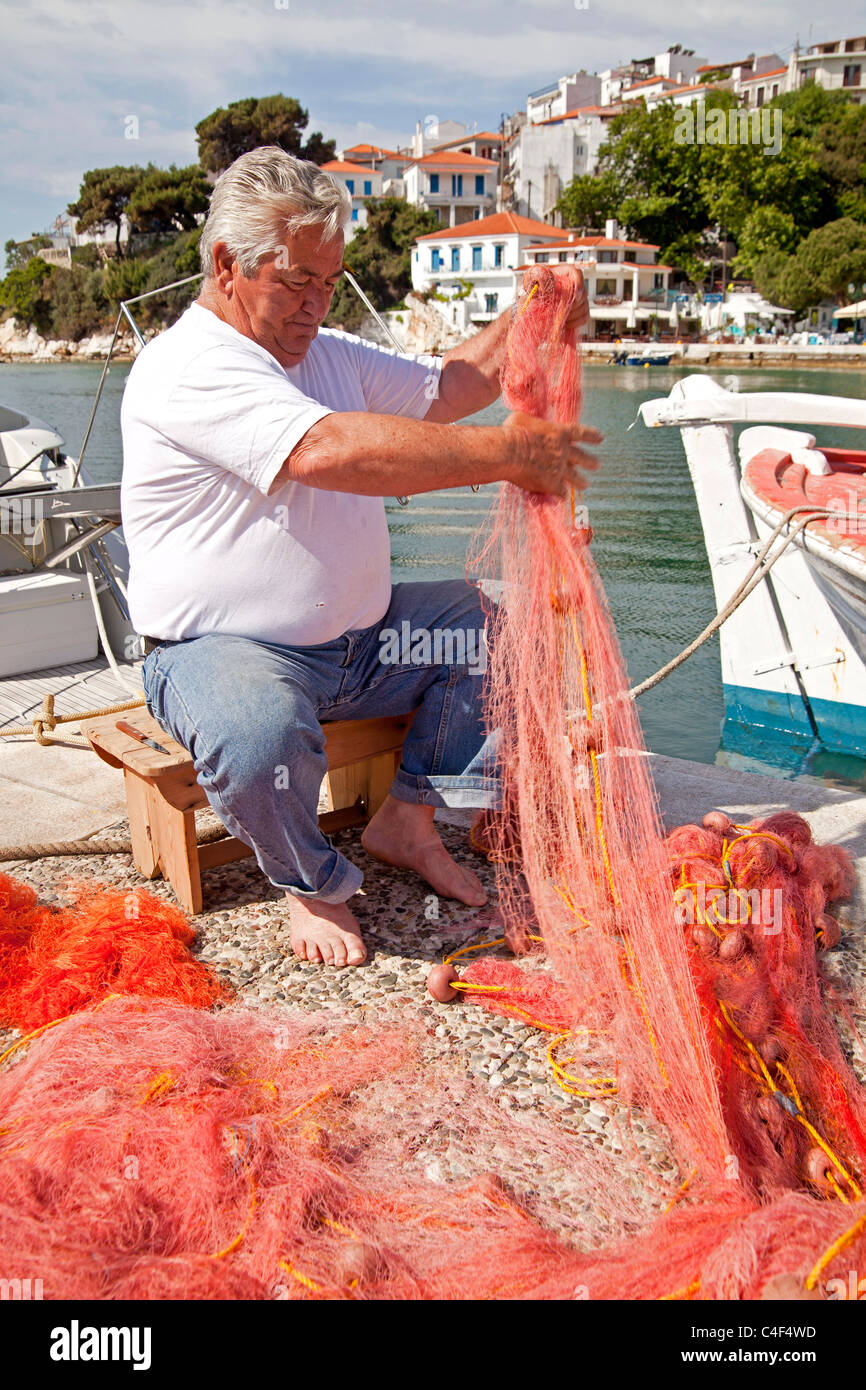 Anziano pescatore riparando il suo net presso il vecchio porto di Skiathos, isola Skiathos, Sporadi settentrionali, Grecia Foto Stock