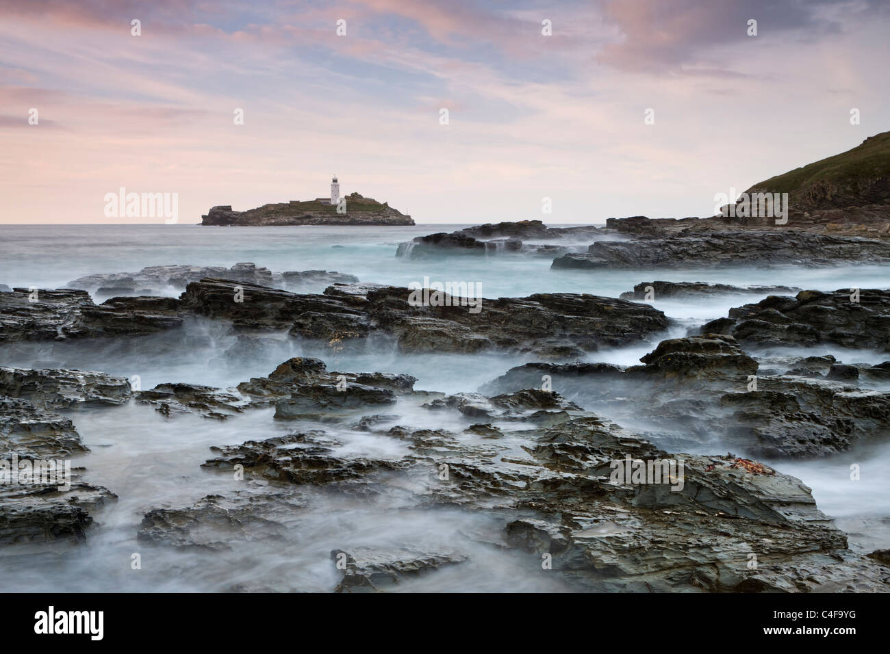 Onde infrangersi sulle rocce di Godrevy Point al tramonto, guardando verso Godrevy Lighthouse, Cornwall, Inghilterra. Foto Stock