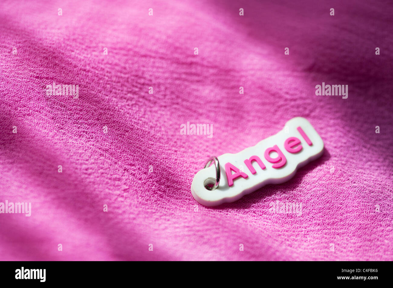 Angelo Rosa tag di plastica su un tessuto rosa sfondo nella luce del sole Foto Stock