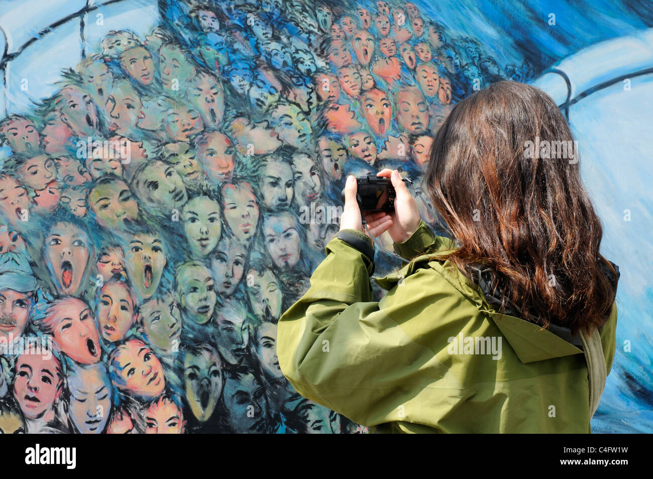 Una donna di scattare le foto dei dipinti sul muro di Berlino presso la East Side Gallery Foto Stock