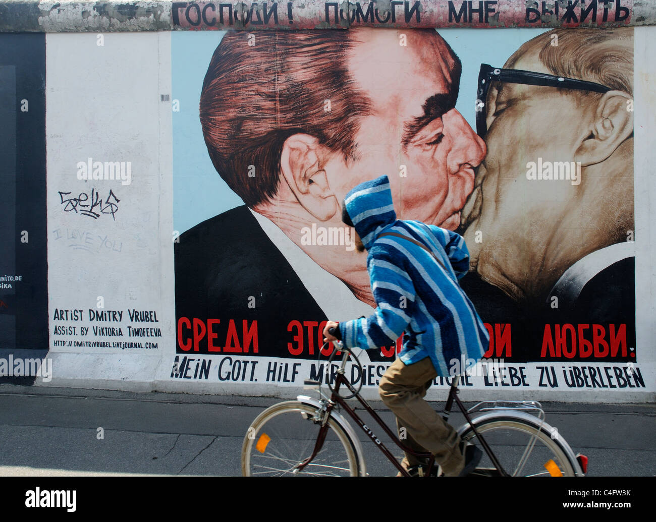 Un ciclista dal famoso dipinto di Honecker Brezhnev e baciare francese sul muro di Berlino a Eastside Gallery Berlin Foto Stock