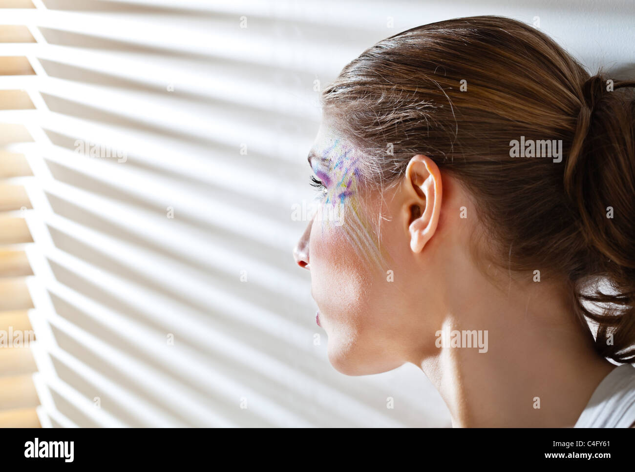 Piuttosto giovane donna magra illuminata dalla luce del sole proveniente attraverso le persiane Foto Stock