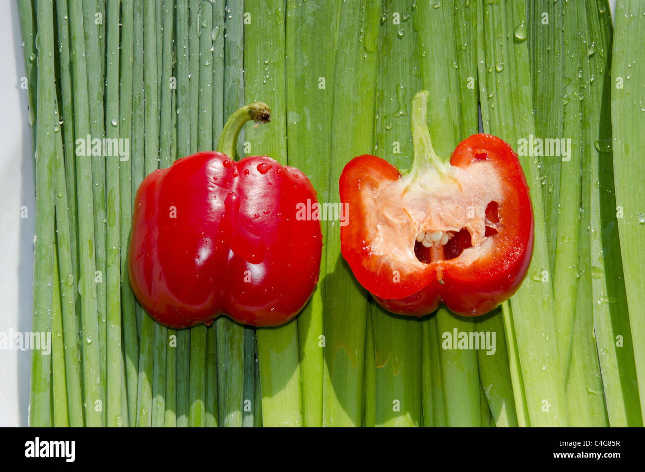 Due fat paprikas rosso sulla fila di orions verde. Uno di loro tagliata nel mezzo. Foto Stock