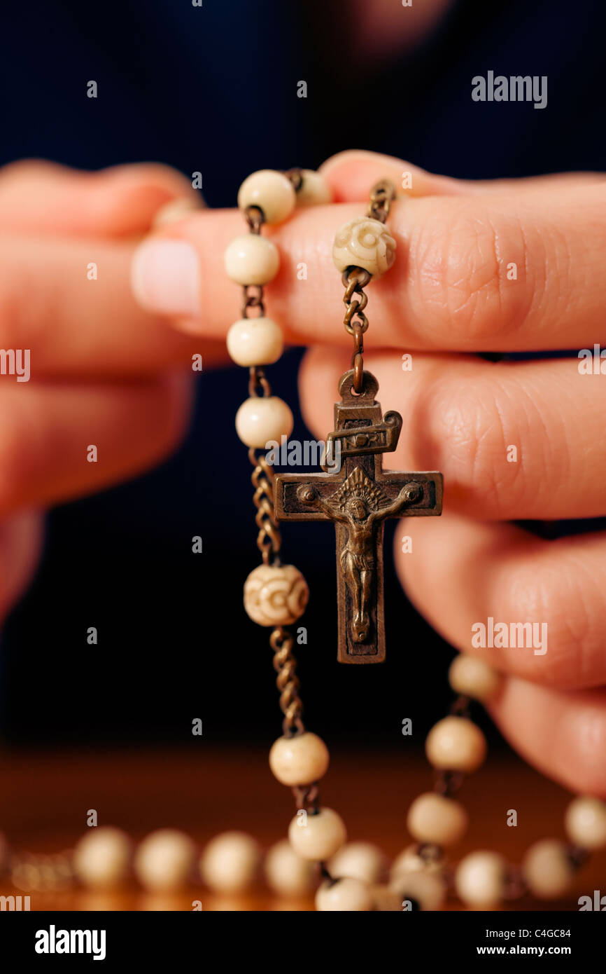 Donna (solo close-up di mani per essere visto) con rosario inviando una preghiera a Dio, l'impostazione Scuro suggerisce lei è triste o lonely Foto Stock