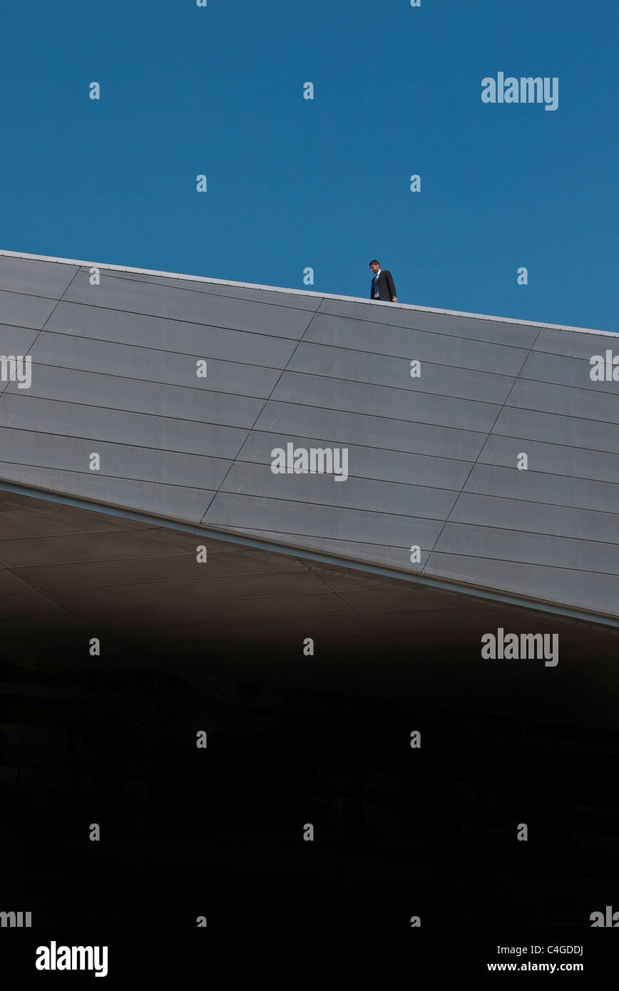 In una veduta distante un uomo è isolato sul tetto del mondo BMW a Monaco di Baviera, in Germania con la testa in giù nel profondo del pensiero. Foto Stock