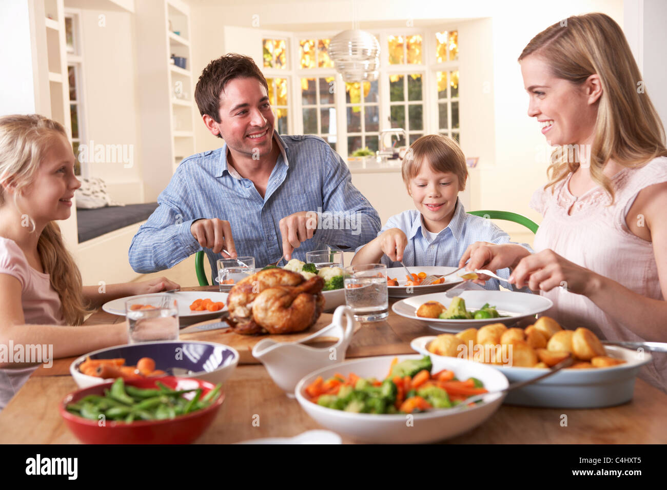La famiglia felice avente pollo arrosto cena a tavola Foto Stock