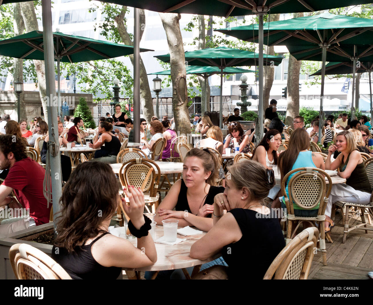 Gruppi di persone a gustare pasti al fresco ombreggiato da ombrelloni a outdoor cafe in Bryant Park Manhattan New York City Foto Stock
