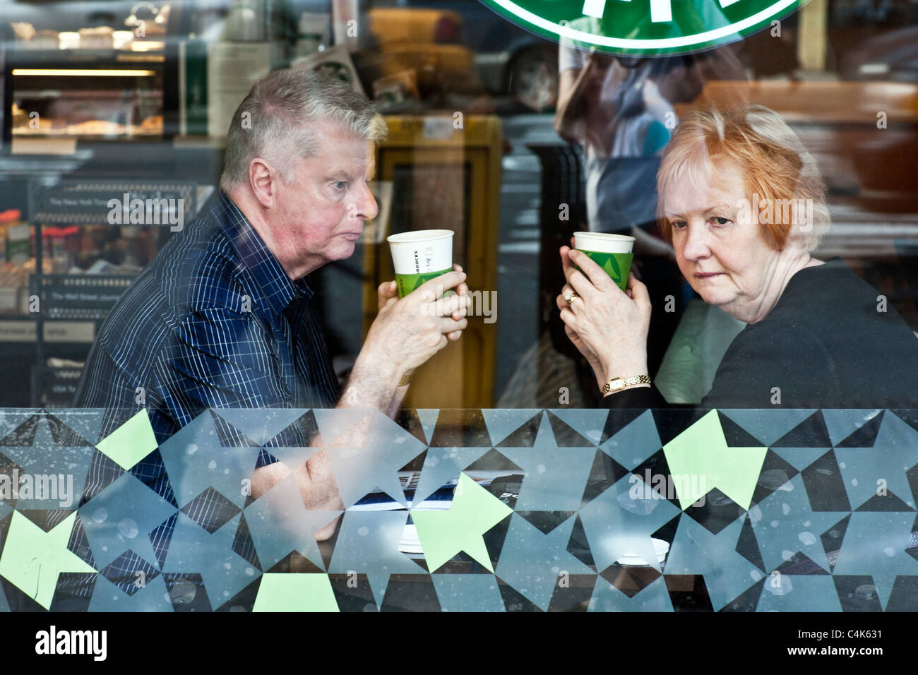 Malinconici coppia senior perso nel pensiero intravisto attraverso la finestra di Starbucks cafe Manhattan New York City Foto Stock