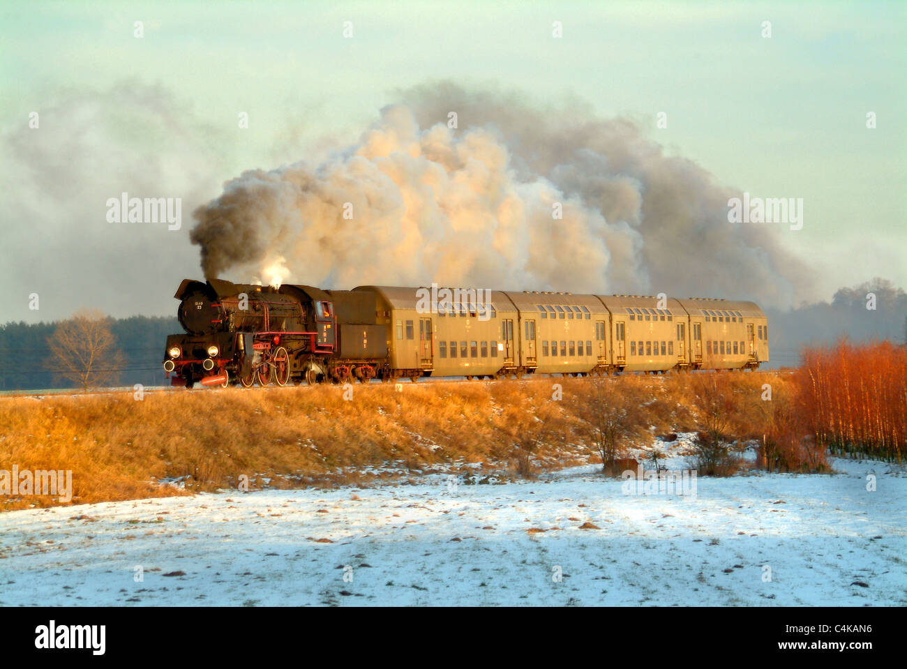 Sole di sera la cattura il vapore loco e carrelli che si innalza su una banca sopra coperta di neve i campi. Foto Stock