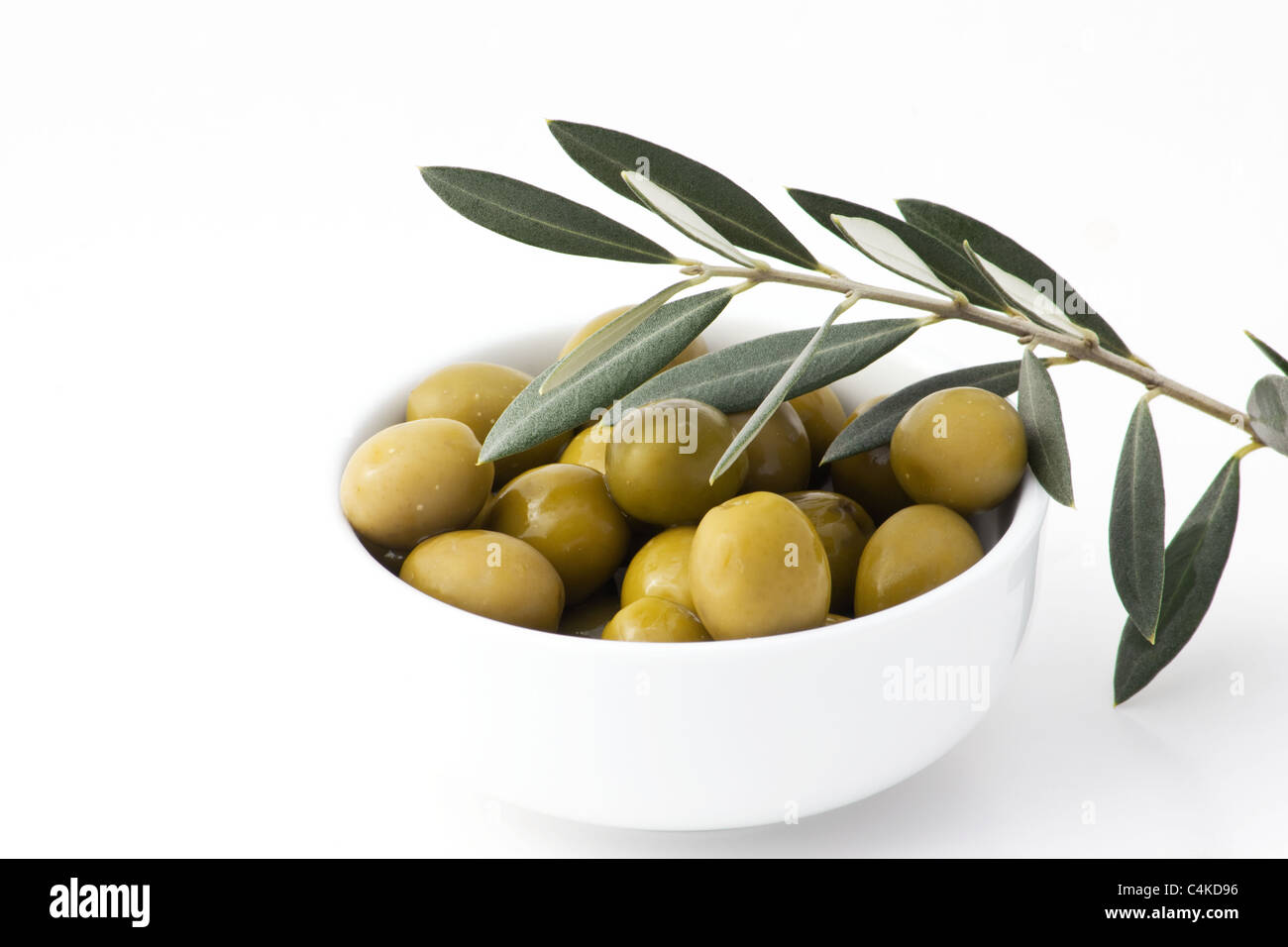 Close-up di olive in una ciotola bianco e foglie su sfondo bianco Foto Stock